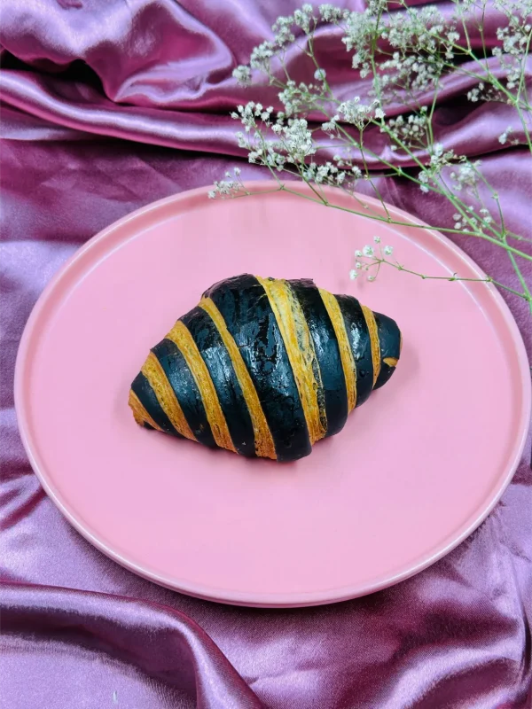 Chocolate Croissant - Golden croissant with chocolate drizzle on pink plate