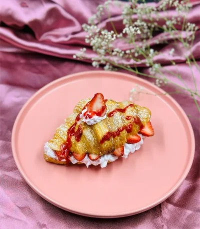Golden baked croissant with strawberry garnish and powdered sugar